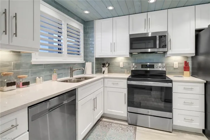 Kitchen with light hardwood / wood-style floors, white cabinetry, backsplash, and stainless steel appliances