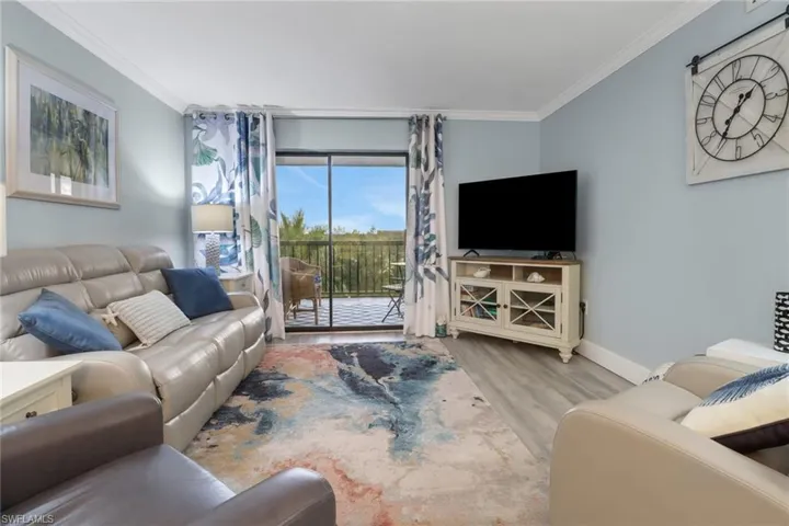 Living room with light wood-type flooring, ornamental molding, and a wall of windows