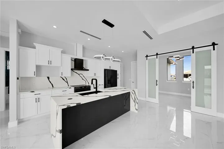 Kitchen with light tile patterned flooring, an island with sink, wall chimney exhaust hood, black fridge with ice dispenser, and a barn door