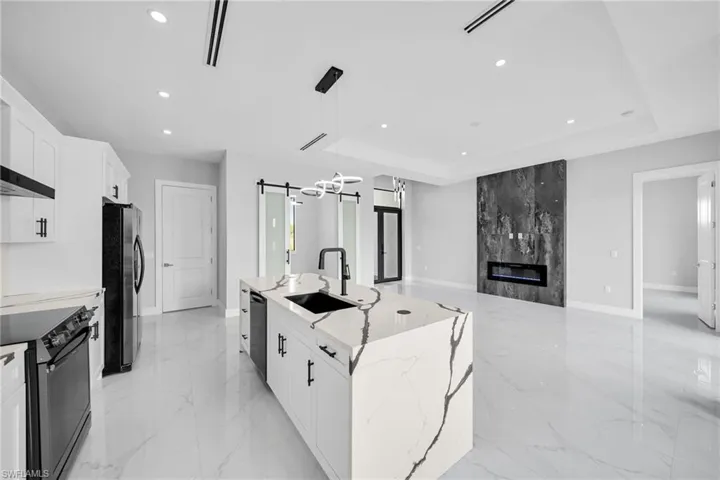 Kitchen featuring black electric range, a tray ceiling, stainless steel refrigerator, and an island with sink