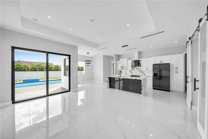 Kitchen featuring a barn door, stainless steel refrigerator with ice dispenser, light tile patterned floors, and a tray ceiling