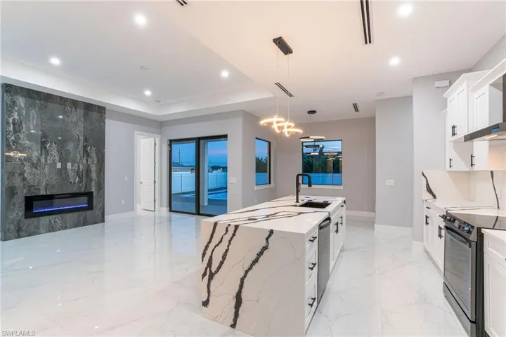Kitchen featuring white cabinets, electric range oven, light stone countertops, pendant lighting, and sink