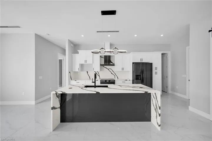 Kitchen with hanging light fixtures, light tile patterned flooring, white cabinetry, and stainless steel fridge with ice dispenser