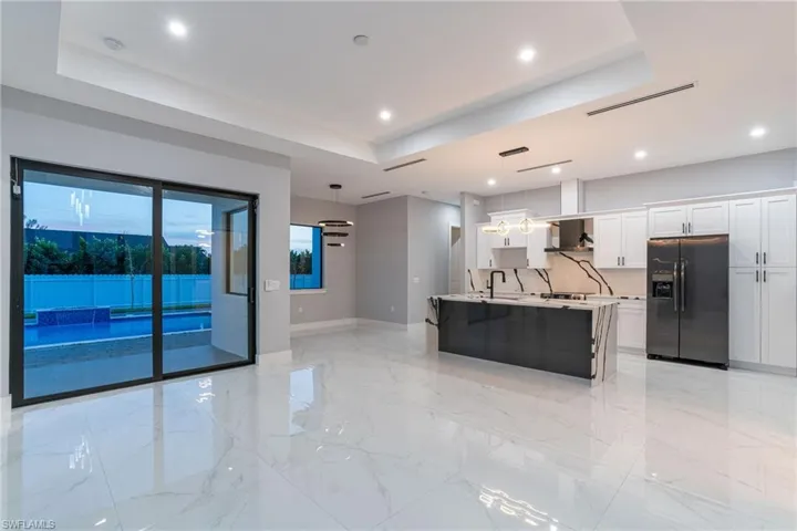 Kitchen featuring a kitchen island with sink, decorative light fixtures, a raised ceiling, and black refrigerator with ice dispenser