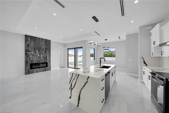 Kitchen featuring decorative light fixtures, an island with sink, a raised ceiling, appliances with stainless steel finishes, and light tile patterned floors