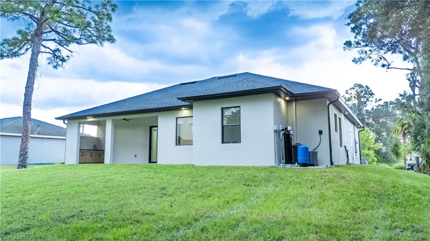 Expansive green lawn surrounds a stucco-finished residence with a dark shingle roof