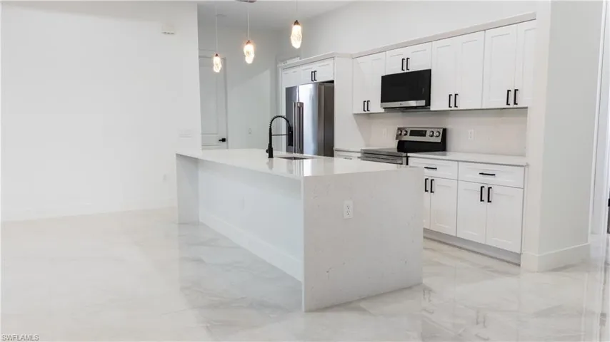 Spacious kitchen featuring an expansive island with a waterfall countertop, white shaker cabinetry, stainless steel appliances, and pendant lighting