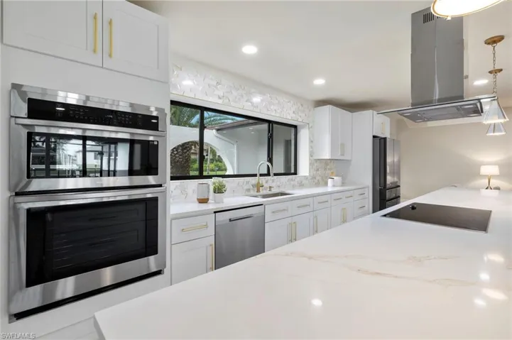 Kitchen featuring white cabinets, decorative backsplash, pendant lighting, appliances with stainless steel finishes, and island range hood