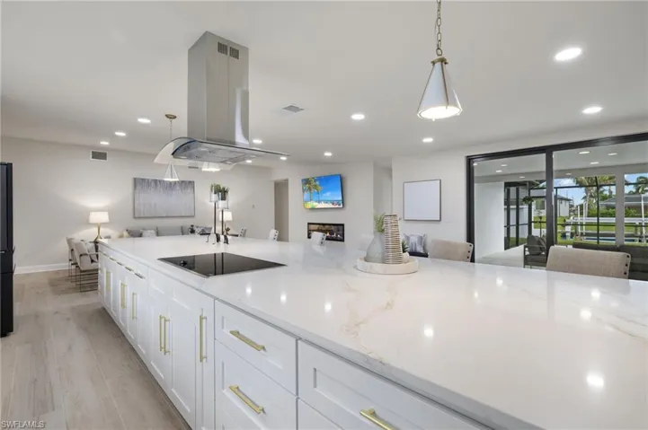 Kitchen with black electric cooktop, white cabinetry, light stone countertops, light hardwood / wood-style flooring, and island range hood