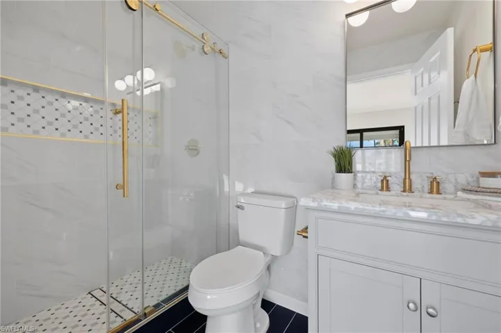 Bathroom with vanity, tile patterned floors, walk in shower, tile walls, and toilet