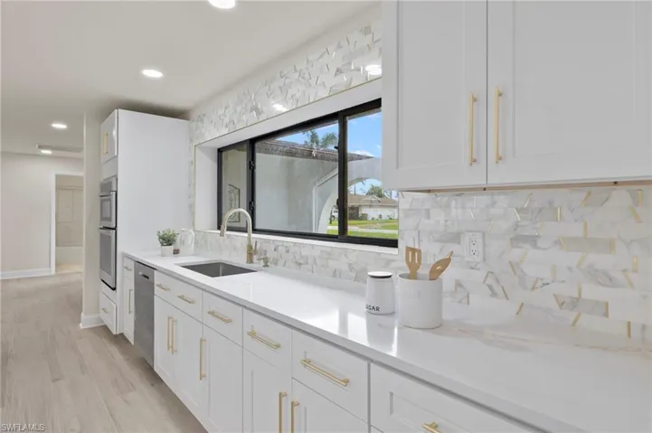 Kitchen featuring sink, light wood-type flooring, white cabinets, and backsplash