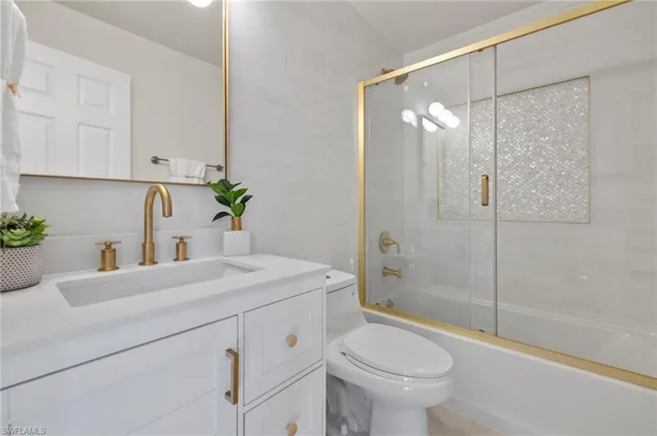 Full bathroom featuring vanity, toilet, enclosed tub / shower combo, and tile walls