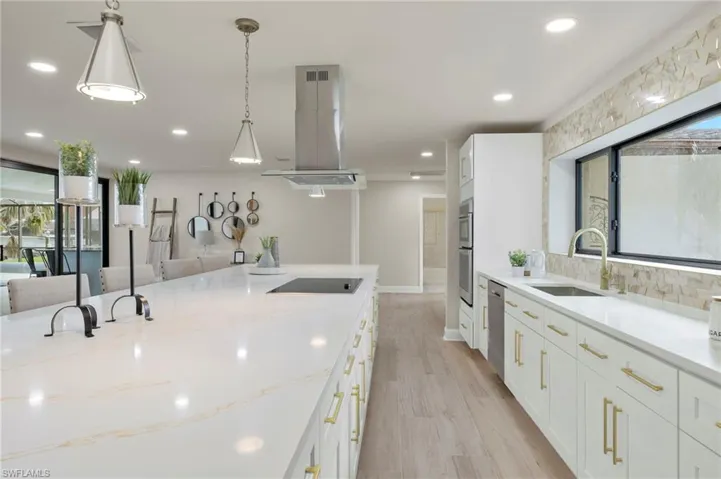 Kitchen with white cabinetry, light wood-type flooring, stainless steel appliances, island exhaust hood, and sink