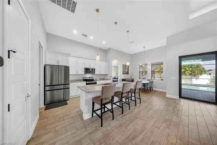 Kitchen featuring stainless steel appliances, white cabinets, light stone countertops, a kitchen bar, and a kitchen island with sink