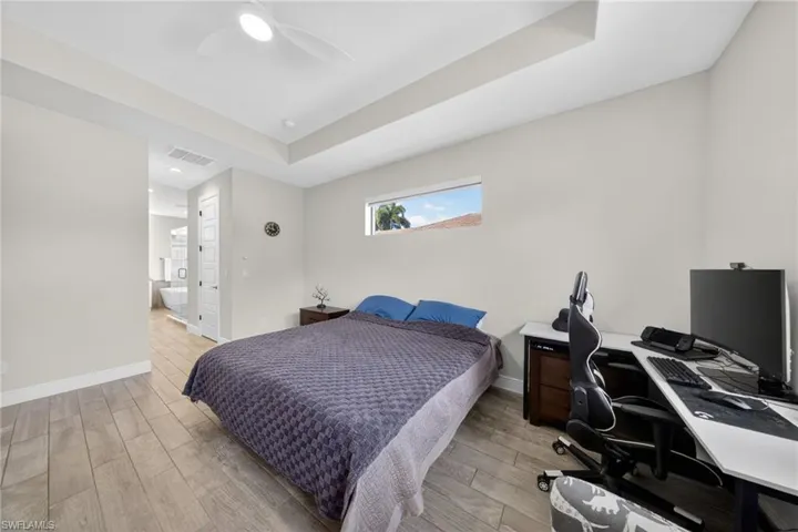 Bedroom with a desk, wood tiled floors, connected bathroom, a raised ceiling, and a ceiling fan
