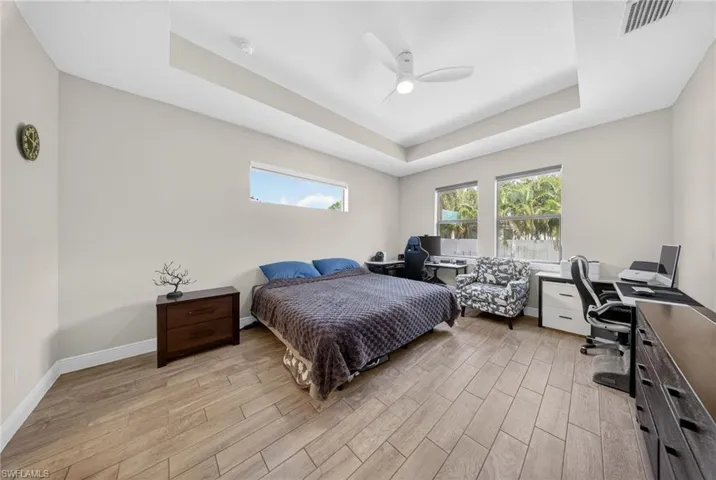 Bedroom featuring a desk, a raised ceiling, wood finish floors, and a ceiling fan
