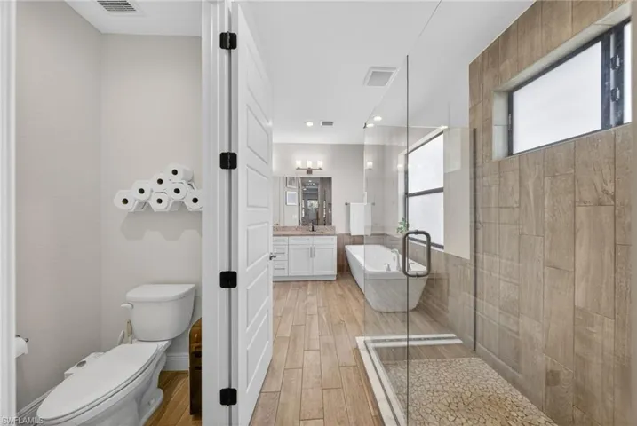 Bathroom featuring walk in shower, vanity, wood finish floors, and a soaking tub
