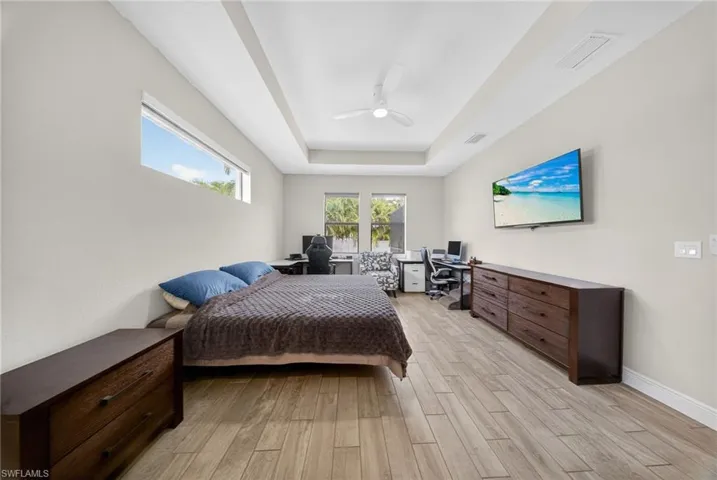 Bedroom featuring a desk, a raised ceiling, light wood-style floors, and ceiling fan