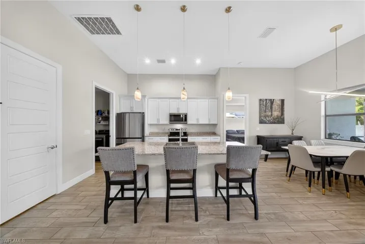 Kitchen with wood tiled floors, a breakfast bar area, white cabinetry, stainless steel appliances, and a center island with sink