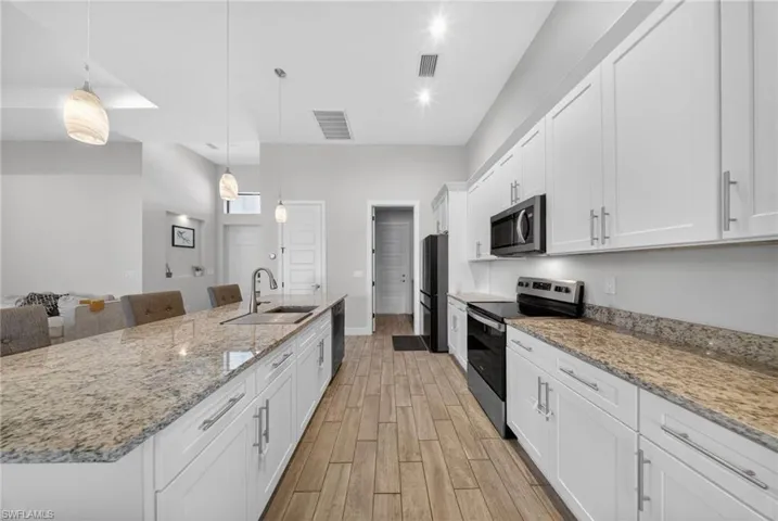 Kitchen featuring white cabinets, stainless steel appliances, light stone counters, and a large island