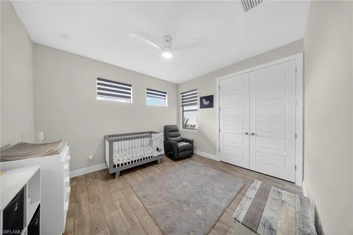 Bedroom with a nursery area, light wood-style floors, a ceiling fan, and a closet