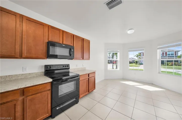 Kitchen featuring black appliances, brown cabinets, light countertops, and light tile patterned flooring