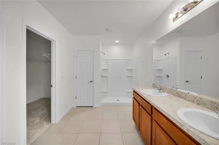 Bathroom with double vanity, a shower stall, light tile patterned floors, a walk in closet, and light carpet