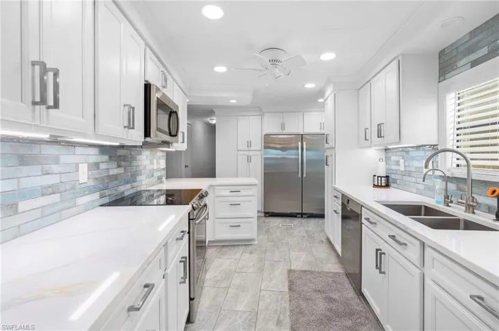 Kitchen featuring appliances with stainless steel finishes, tasteful backsplash, light stone counters, sink, and white cabinets