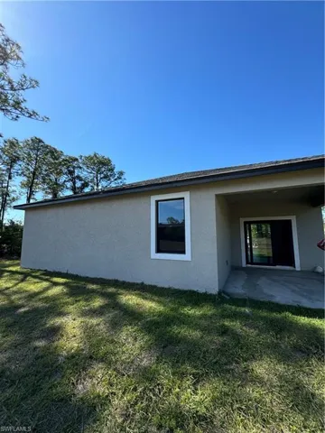 Rear view of house with a lawn, stucco siding, and a patio