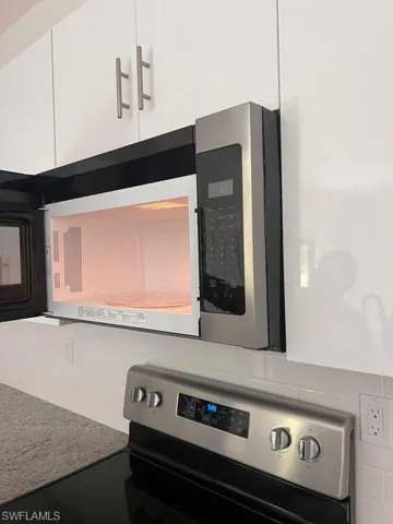 Kitchen view of stainless steel appliances, white cabinetry, and light stone counters