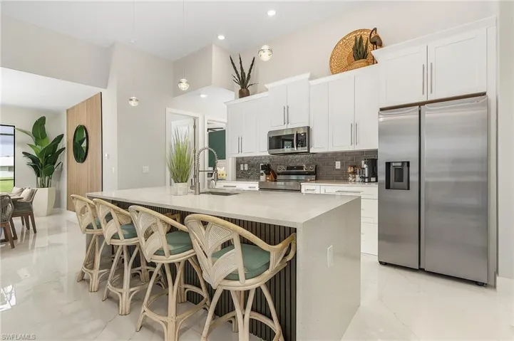 Kitchen with decorative backsplash, a center island with sink, white cabinets, a sink, and appliances with stainless steel finishes.