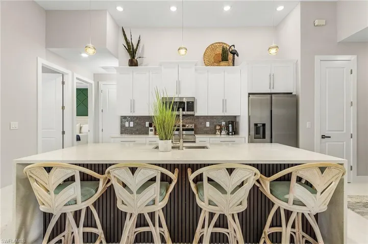 Kitchen featuring white cabinets, a sink, stainless steel appliances, a large island with sink, and tasteful backsplash