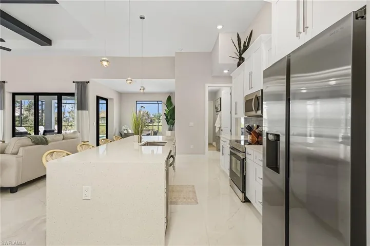 Kitchen with marble finish floor, open floor plan, white cabinetry, a sink, and stainless steel appliances.