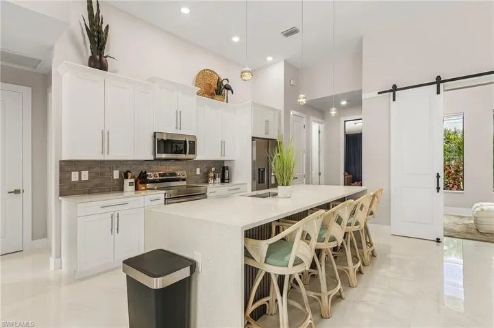 Kitchen featuring island with sink, white cabinets, stainless steel appliances. Quartz water fall counter tops.