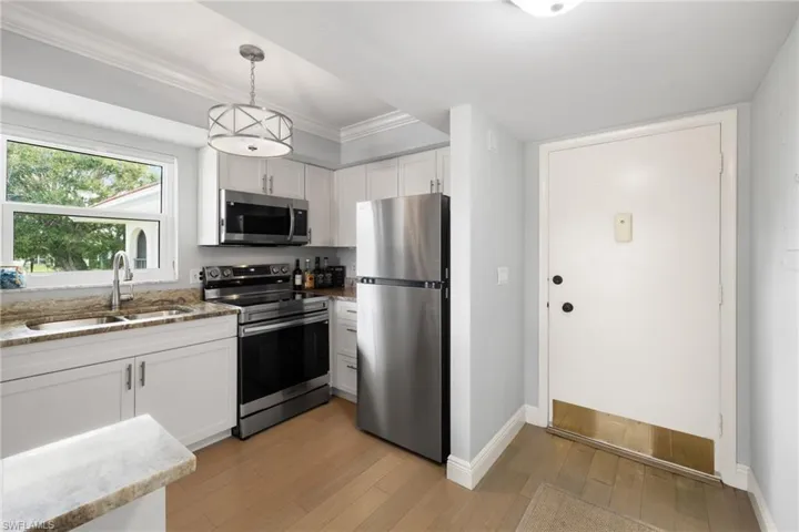 Kitchen with stainless steel appliances, light stone counters, white cabinetry, light wood-style floors, and decorative light fixtures