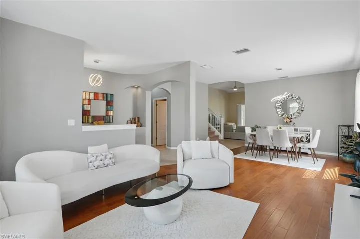 Living room with wood finished floors, visible vents, baseboards, stairway, and arched walkways