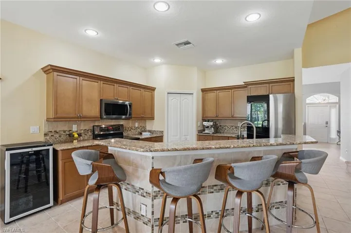 Kitchen featuring brown cabinetry, stainless steel appliances, light tile patterned floors, and beverage cooler