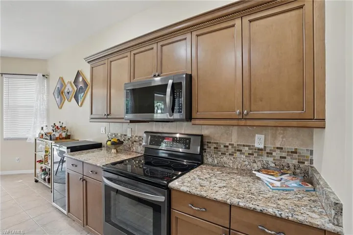 Kitchen featuring light tile patterned floors, baseboards, appliances with stainless steel finishes, and decorative backsplash