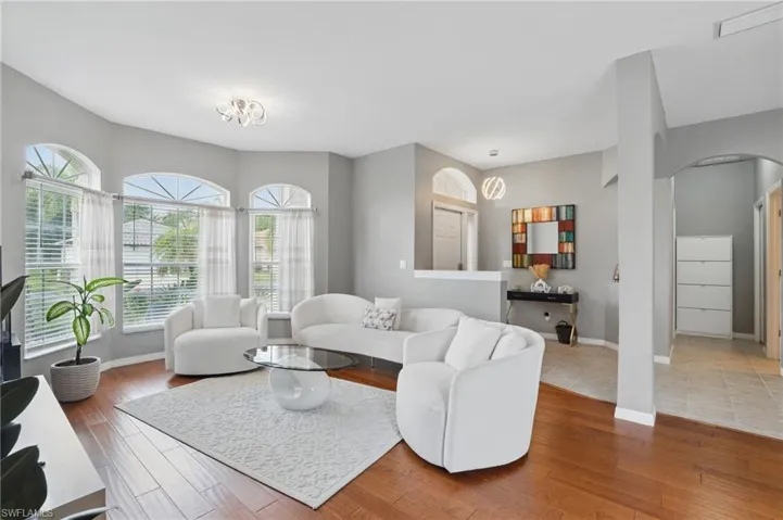 Living room featuring a wealth of natural light, arched walkways, baseboards, and wood finished floors