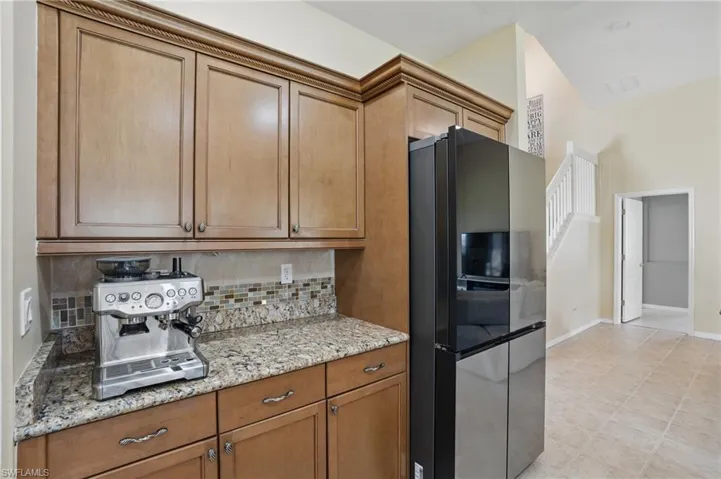 Kitchen featuring brown cabinets, freestanding refrigerator, baseboards, light stone countertops, and tasteful backsplash