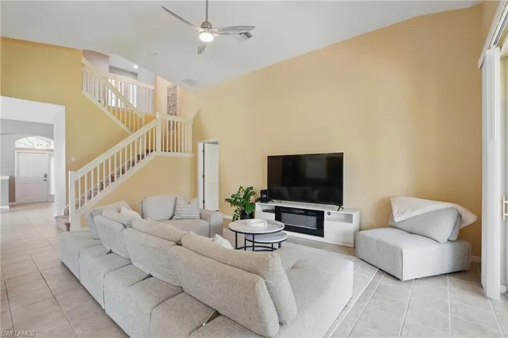 Living area featuring light tile patterned floors, stairs, ceiling fan, and high vaulted ceiling