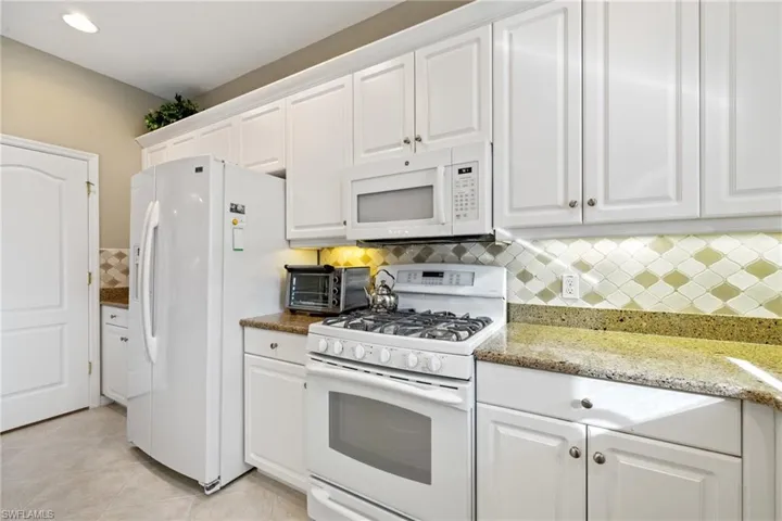 Kitchen with white cabinetry, white appliances, light stone counters, and light tile patterned floors