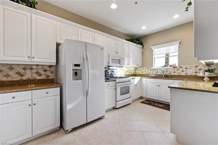 Kitchen featuring sink, white cabinets, decorative backsplash, dark stone counters, and white appliances
