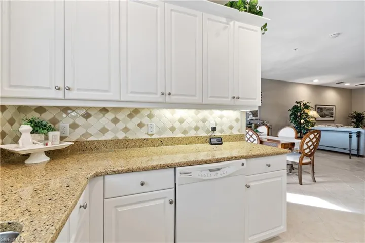 Kitchen featuring white cabinetry, dishwasher, decorative backsplash, light tile patterned floors, and light stone counters