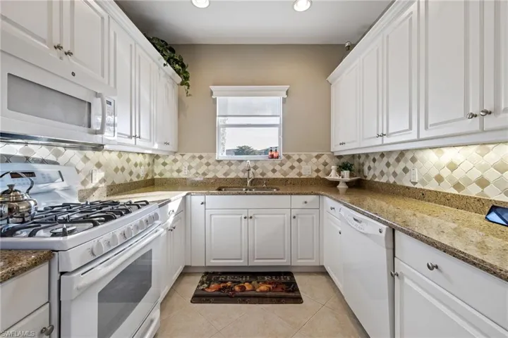 Kitchen featuring sink, white cabinetry, stone countertops, light tile patterned floors, and white appliances