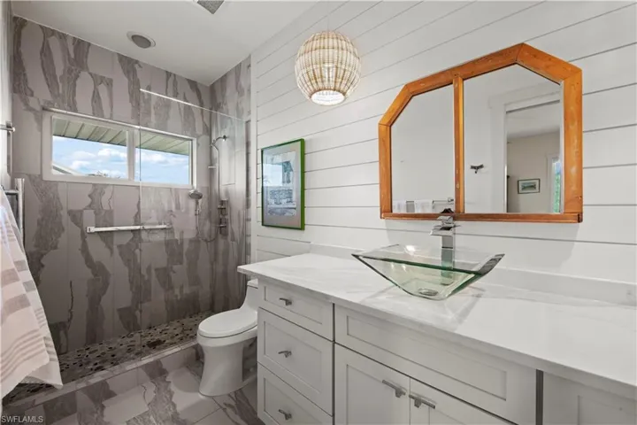 Bathroom with vanity, toilet, tiled shower, and wood walls