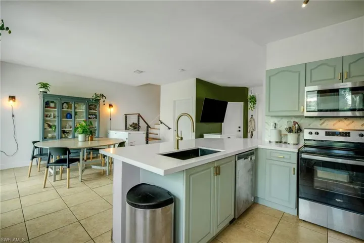 Kitchen featuring stainless steel appliances, kitchen peninsula, sink, tasteful backsplash, and light tile flooring