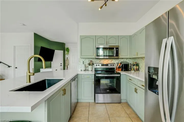 Kitchen featuring kitchen peninsula, tasteful backsplash, light tile flooring, sink, and appliances with stainless steel finishes