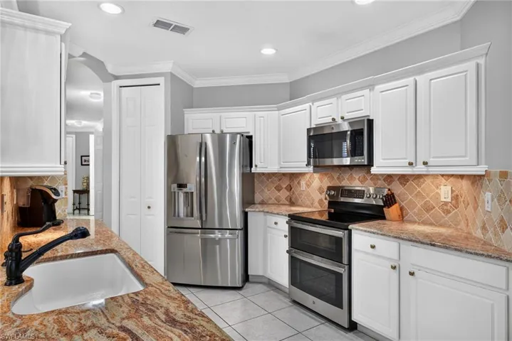 Kitchen featuring white cabinetry, stone-finish countertops, stainless steel appliances, ceramic tile backsplash, and an undermount sink with a dark-finish faucet
