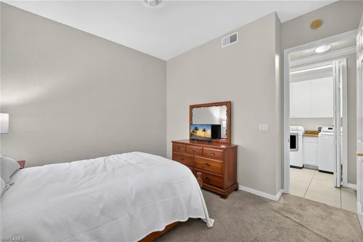 Neutral-toned interior featuring wall-to-wall carpeting and access to a laundry area with white cabinetry and tile flooring